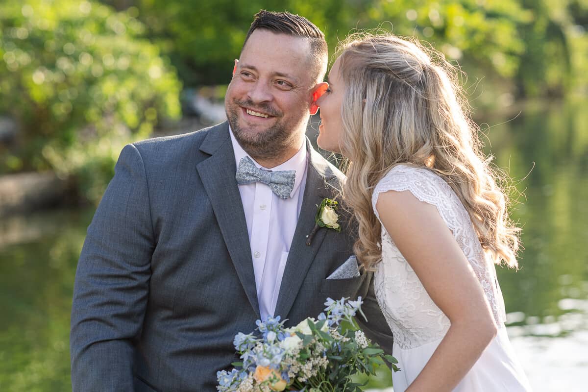 Bride whispers in the ear of her groom during golden hour sunset